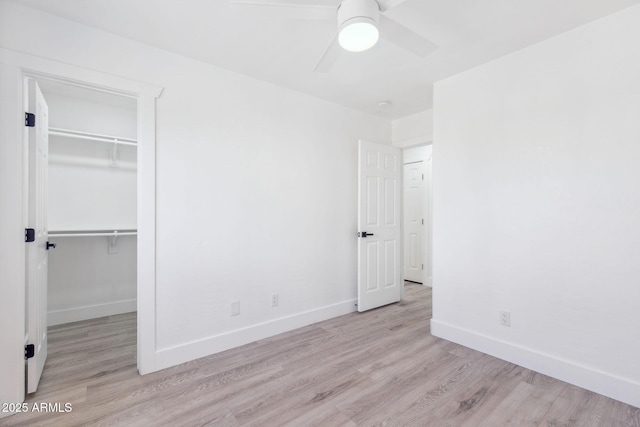unfurnished bedroom with baseboards, a spacious closet, light wood finished floors, and a closet
