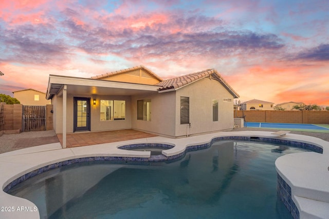 back of property at dusk featuring a fenced in pool, an in ground hot tub, stucco siding, and a tiled roof