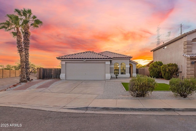 mediterranean / spanish-style home featuring stucco siding, a tiled roof, fence, and a garage