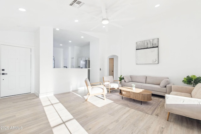 living room featuring arched walkways, a ceiling fan, visible vents, and wood finished floors