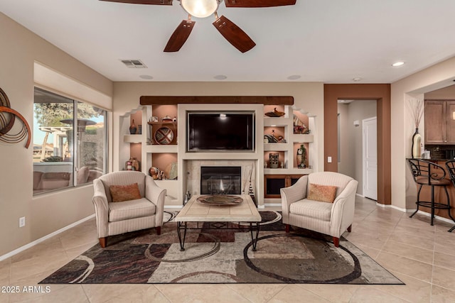 tiled living room featuring ceiling fan, a fireplace, and built in shelves