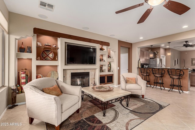 living room with a tiled fireplace, light tile patterned floors, built in features, and ceiling fan