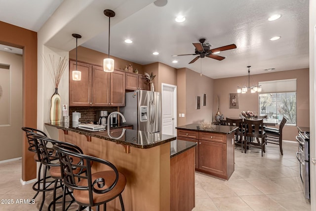 kitchen featuring appliances with stainless steel finishes, decorative light fixtures, a breakfast bar area, dark stone counters, and kitchen peninsula