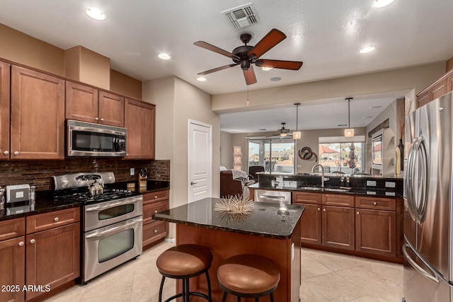 kitchen featuring sink, stainless steel appliances, a center island, a kitchen bar, and decorative light fixtures