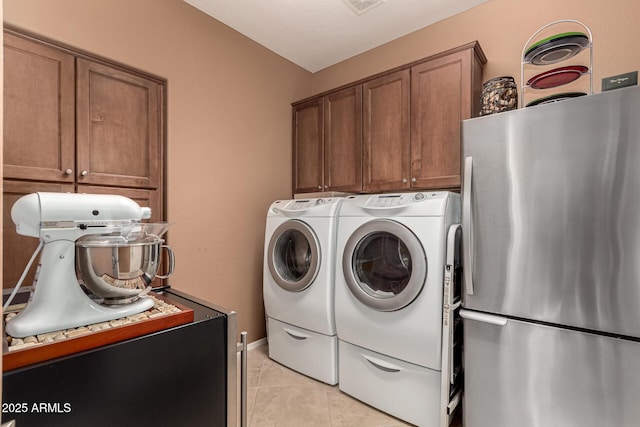 clothes washing area with cabinets, light tile patterned floors, and washing machine and clothes dryer