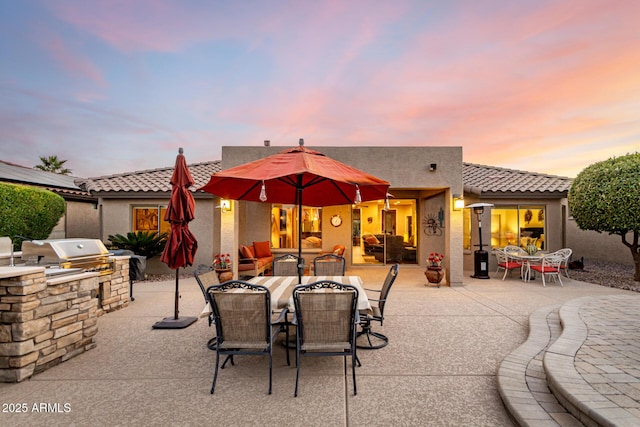 patio terrace at dusk with an outdoor kitchen and area for grilling