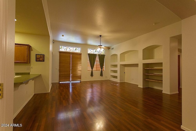 unfurnished living room featuring built in shelves, ceiling fan, and dark hardwood / wood-style flooring