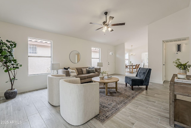 living room with plenty of natural light, ceiling fan with notable chandelier, baseboards, and light wood-style floors