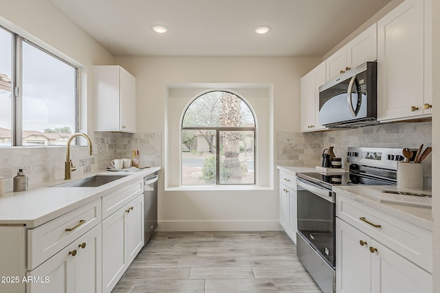 kitchen with a sink, stainless steel appliances, white cabinets, light countertops, and baseboards