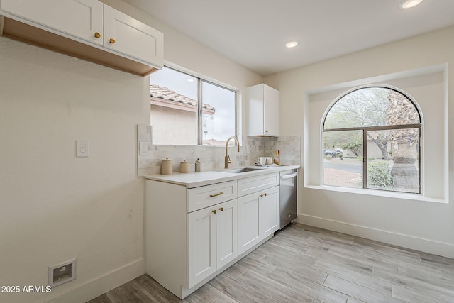 kitchen with light wood finished floors, a sink, light countertops, decorative backsplash, and dishwasher