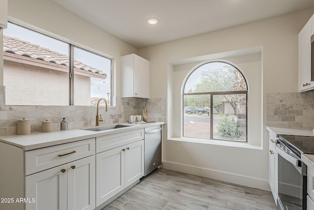 kitchen with baseboards, dishwasher, stainless steel range with electric cooktop, white cabinetry, and a sink