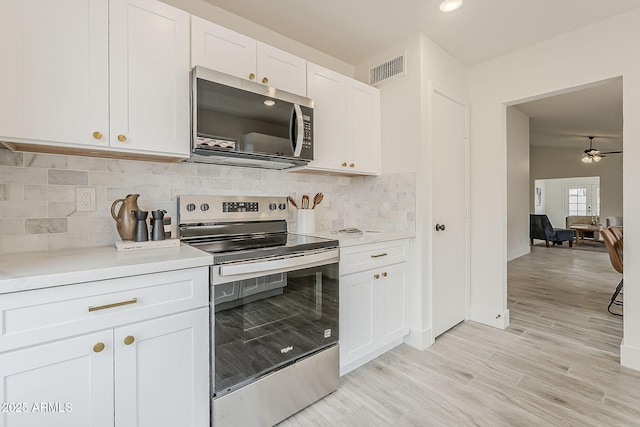 kitchen featuring tasteful backsplash, light countertops, appliances with stainless steel finishes, light wood-style floors, and white cabinetry