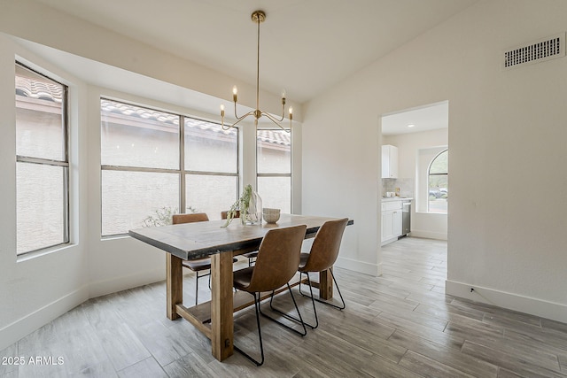 dining area with visible vents, light wood-style floors, baseboards, a chandelier, and vaulted ceiling