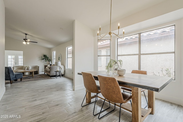 dining area featuring ceiling fan with notable chandelier, baseboards, lofted ceiling, and light wood-style floors