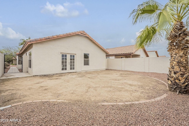 rear view of property with stucco siding, a tiled roof, fence, french doors, and a patio area