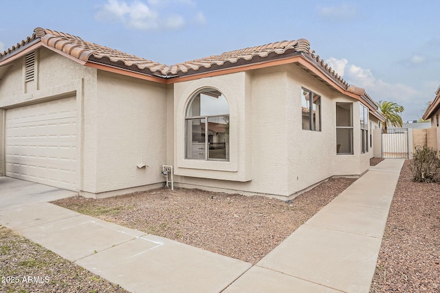 view of home's exterior with fence, stucco siding, concrete driveway, a garage, and a tiled roof