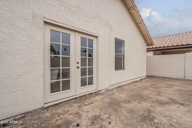 property entrance featuring a tiled roof, french doors, stucco siding, and fence