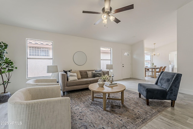 living room featuring vaulted ceiling, ceiling fan with notable chandelier, light wood-type flooring, and baseboards