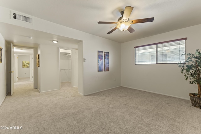 unfurnished bedroom with a closet, a spacious closet, ceiling fan, and light colored carpet