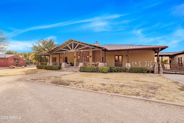 view of front of house featuring metal roof, a chimney, a porch, and stucco siding