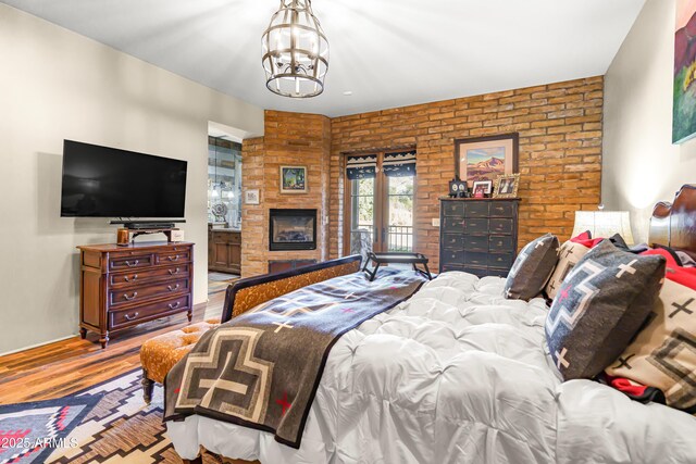 51238 N Pinal Ranch Rd, Miami, AZ 85539 - bedroom with brick wall, a notable chandelier, a fireplace with raised hearth, and wood finished floors