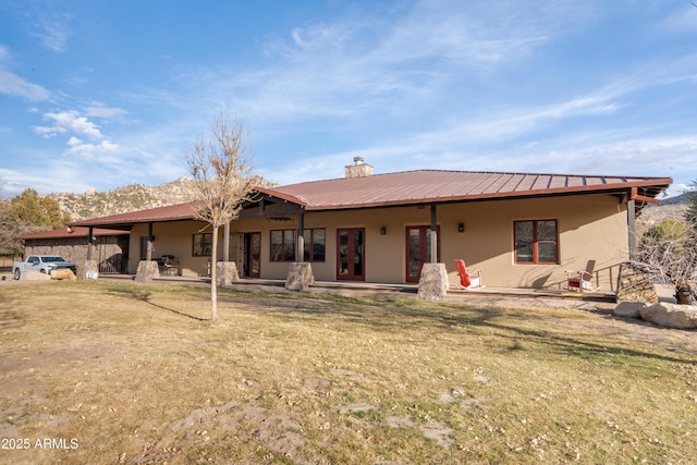 back of house with metal roof, a chimney, a patio area, and stucco siding