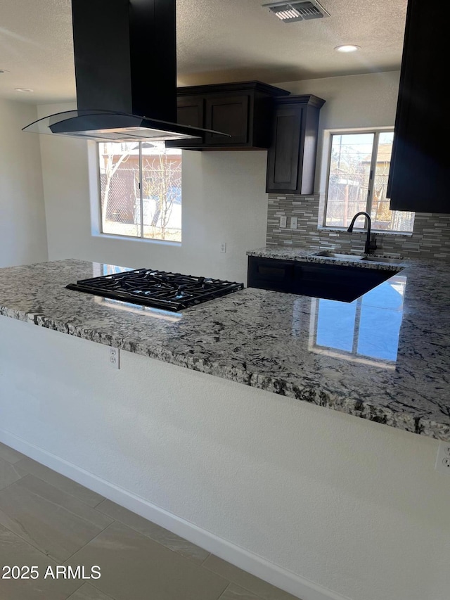 kitchen featuring gas stovetop, island exhaust hood, and light stone countertops