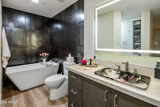 bathroom featuring a freestanding tub, toilet, tile walls, vanity, and wood finished floors