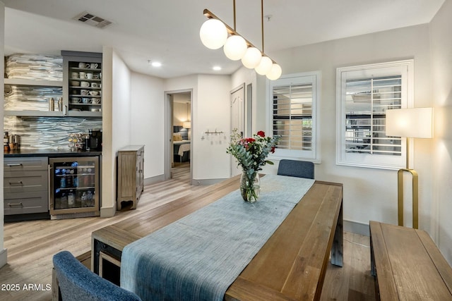 dining space with wine cooler, a dry bar, light wood finished floors, and visible vents