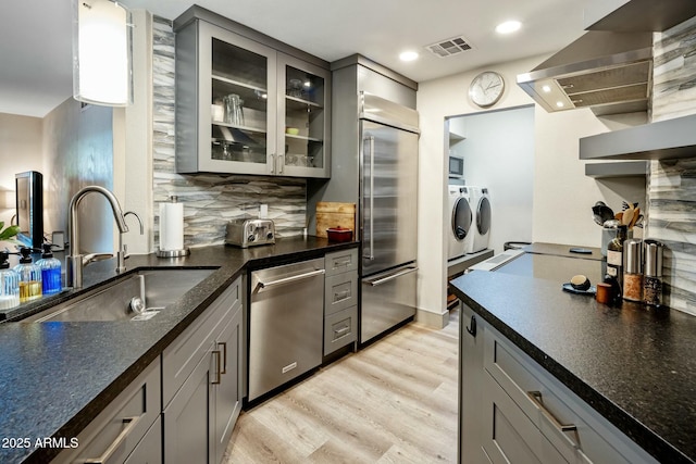 kitchen featuring independent washer and dryer, wall chimney range hood, visible vents, a sink, and stainless steel appliances
