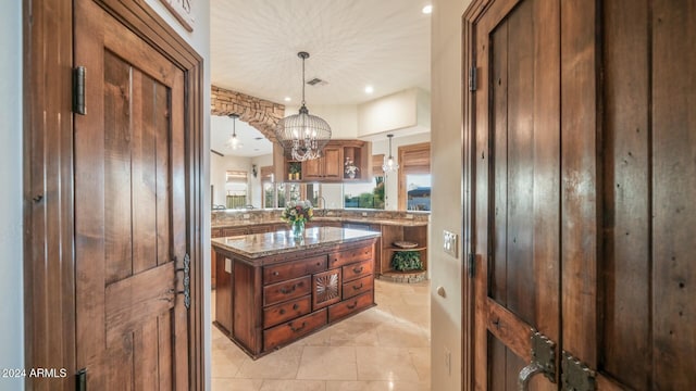 kitchen with a center island, an inviting chandelier, kitchen peninsula, dark stone counters, and pendant lighting