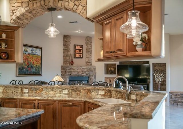 kitchen featuring light stone countertops, sink, hanging light fixtures, kitchen peninsula, and a fireplace