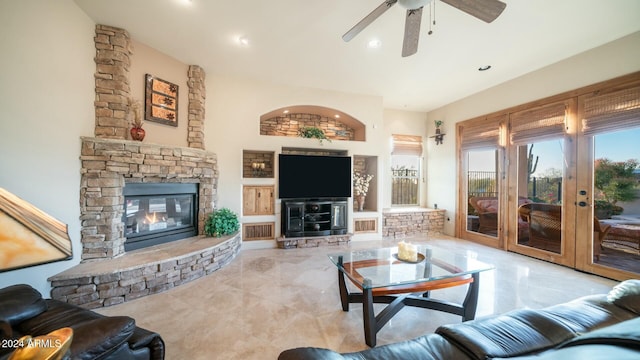 living room with a stone fireplace, ceiling fan, and french doors