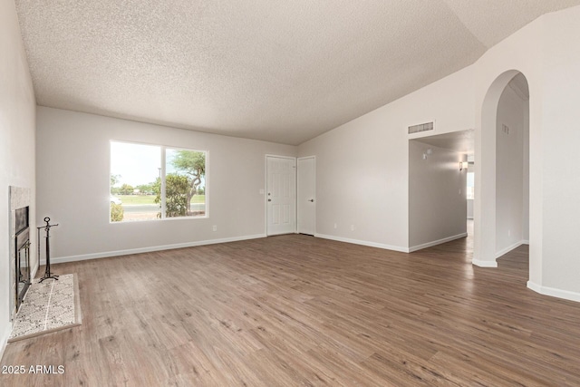 2318 N 87th Ave, Phoenix, AZ 85037 - unfurnished living room with arched walkways, wood finished floors, a textured ceiling, a tile fireplace, and vaulted ceiling