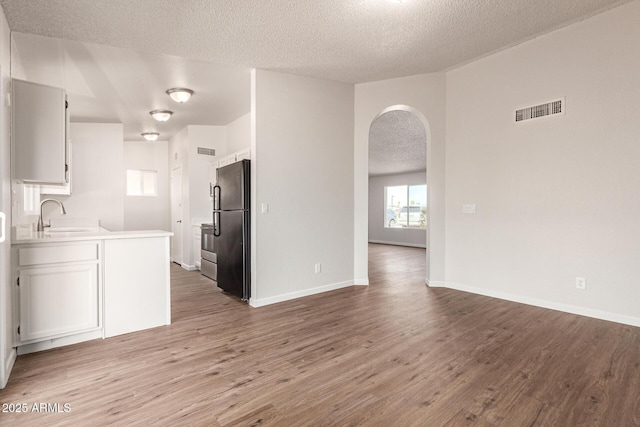 2318 N 87th Ave, Phoenix, AZ 85037 - kitchen featuring freestanding refrigerator, a textured ceiling, arched walkways, wood finished floors, and white cabinetry