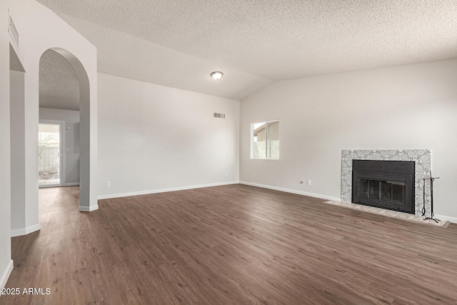 2318 N 87th Ave, Phoenix, AZ 85037 - unfurnished living room featuring dark wood-type flooring, vaulted ceiling, a premium fireplace, arched walkways, and a textured ceiling