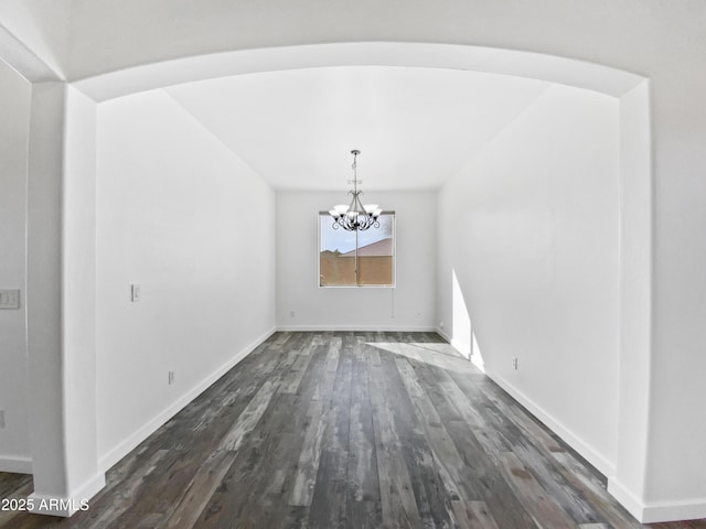 unfurnished dining area with baseboards, arched walkways, a notable chandelier, and dark wood-style flooring