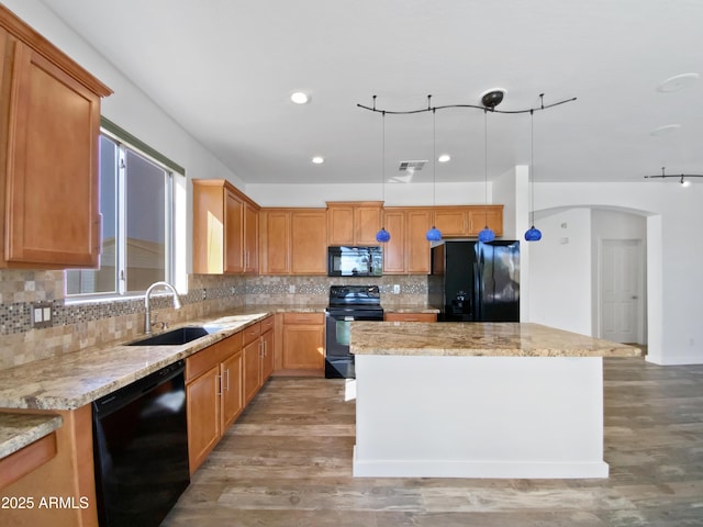 kitchen featuring a sink, decorative backsplash, black appliances, light wood-type flooring, and a center island