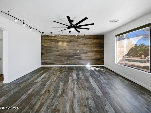 spare room featuring visible vents, wood finished floors, wood walls, baseboards, and an accent wall