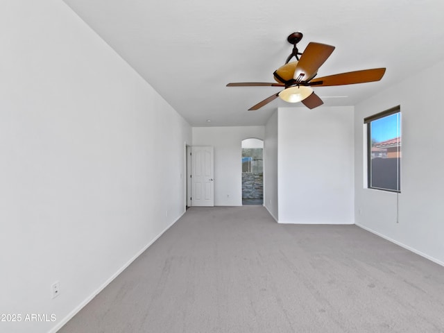 carpeted empty room with a ceiling fan, arched walkways, and baseboards