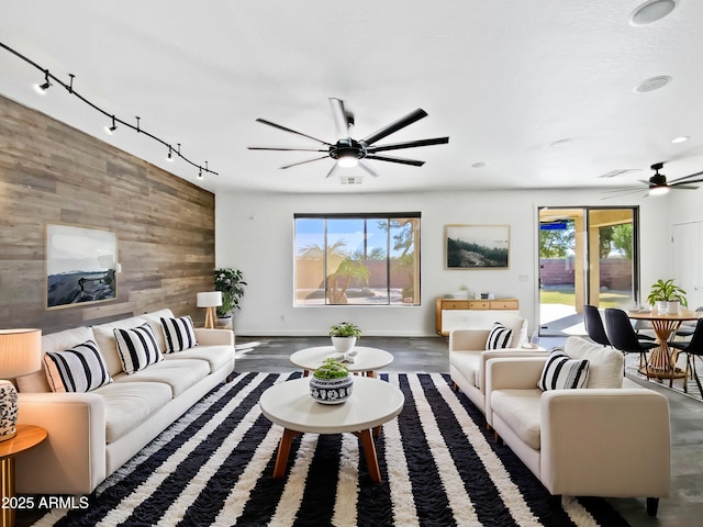 living area with wood walls, a ceiling fan, an accent wall, and a healthy amount of sunlight