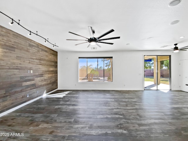 empty room with a ceiling fan, wooden walls, rail lighting, and wood finished floors