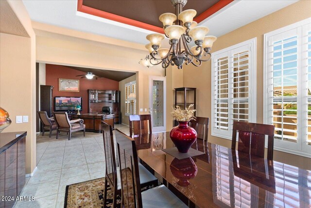 tiled dining space with ceiling fan with notable chandelier, a tray ceiling, and plenty of natural light