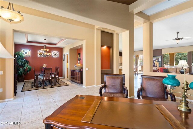 dining room with ceiling fan with notable chandelier, a raised ceiling, and light tile patterned floors