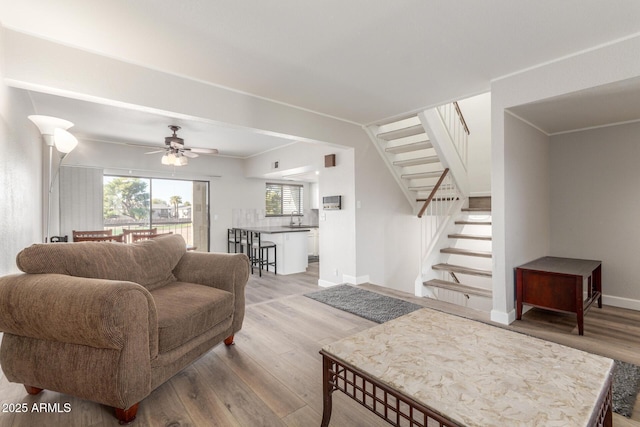 living room featuring ceiling fan, light wood-type flooring, sink, and ornamental molding