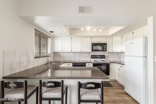 kitchen with black appliances, a raised ceiling, sink, white cabinetry, and a breakfast bar area