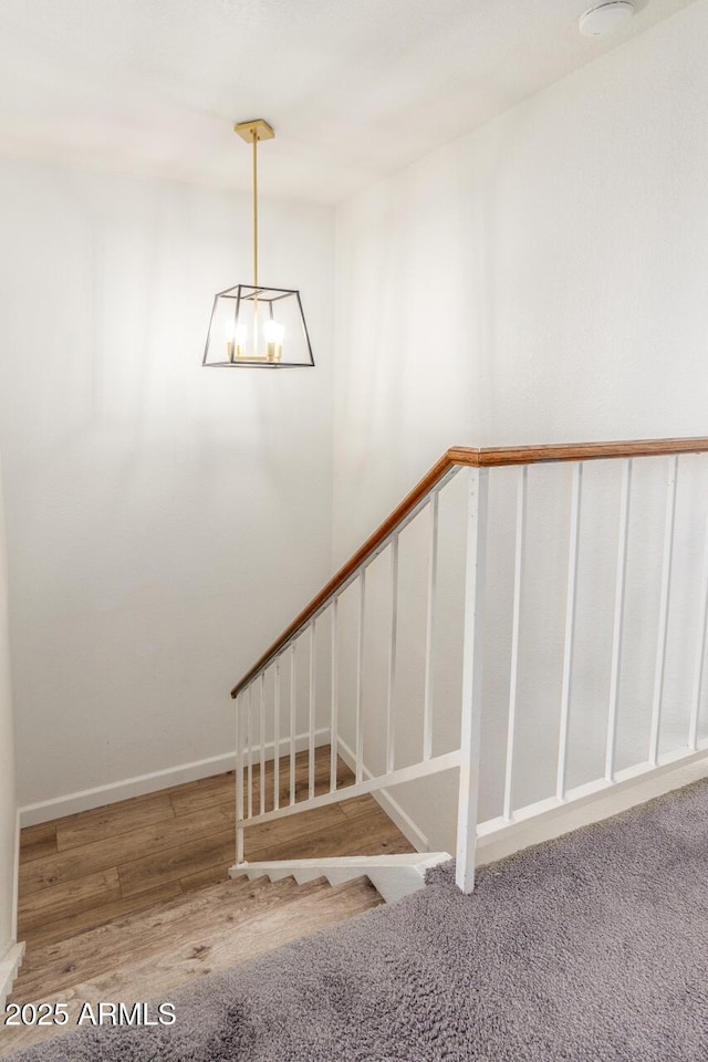 stairway with wood-type flooring and a notable chandelier