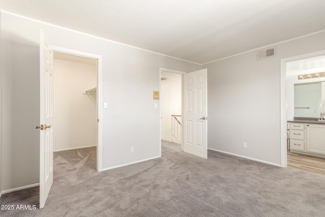 unfurnished bedroom with ensuite bathroom, a closet, a walk in closet, and light colored carpet