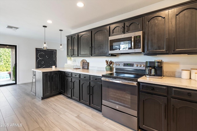 kitchen with appliances with stainless steel finishes, decorative light fixtures, dark brown cabinetry, light hardwood / wood-style flooring, and kitchen peninsula