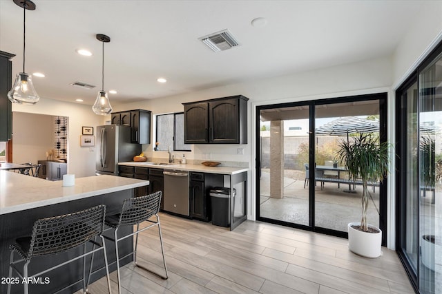 kitchen featuring decorative light fixtures, stainless steel appliances, sink, dark brown cabinets, and a breakfast bar area